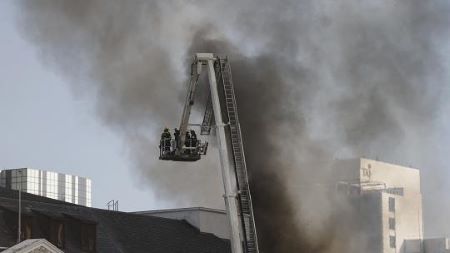 Des pompiers sont vus sur l'échelle d'un camion de pompiers alors que de la fumée s'échappe du toit d'un bâtiment dans le quartier du Parlement sud-africain au Cap - AFP